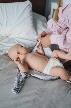 Mother gently dresses infant on bed, showcasing tenderness and care.